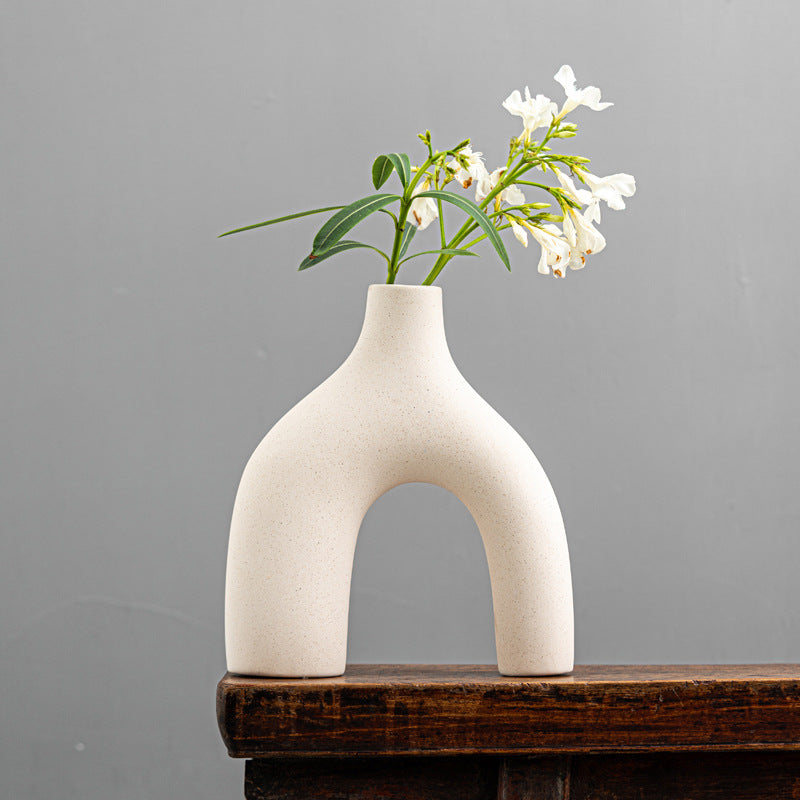 White ceramic vase with flowers on a wooden surface against a gray background