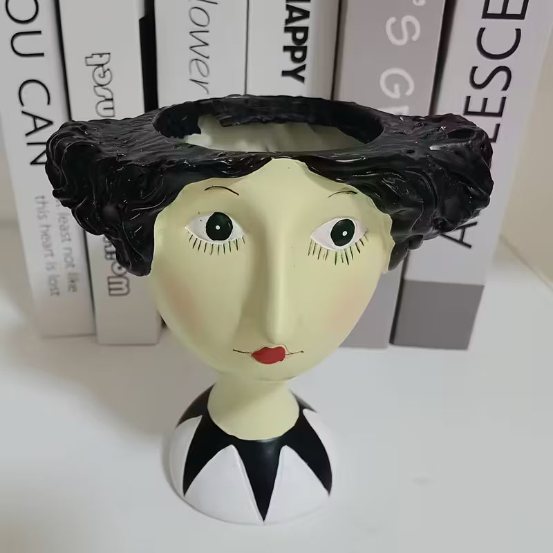 Decorative object resembling a woman's head with black hair and red lips, set against books.