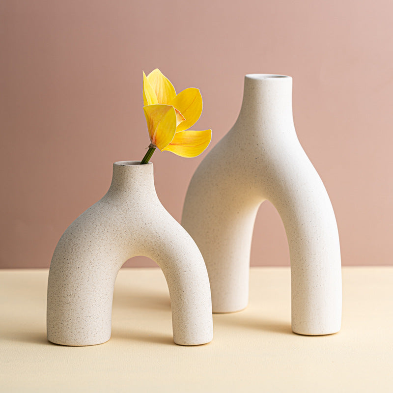 Two white ceramic vases with a yellow tulip against a pink background