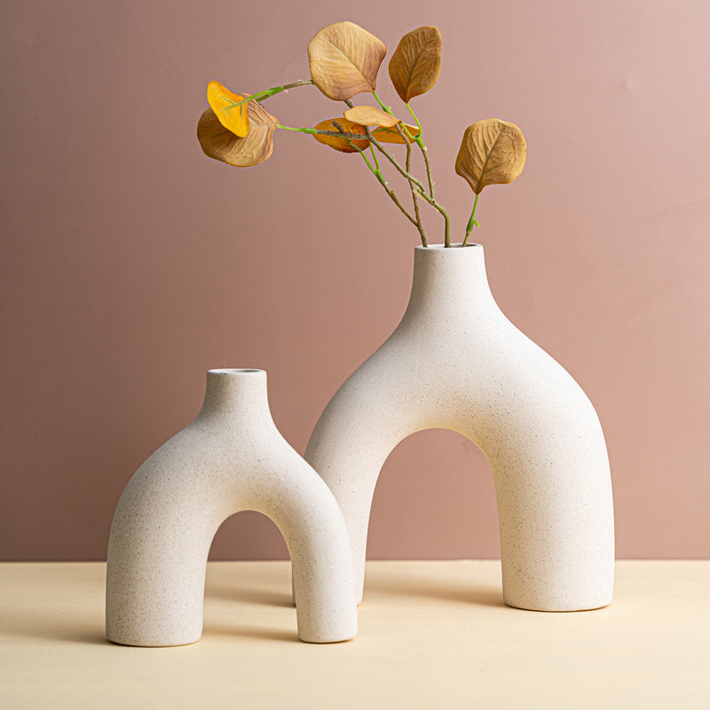 Two white ceramic vases with arch designs on a beige surface against a pink background
