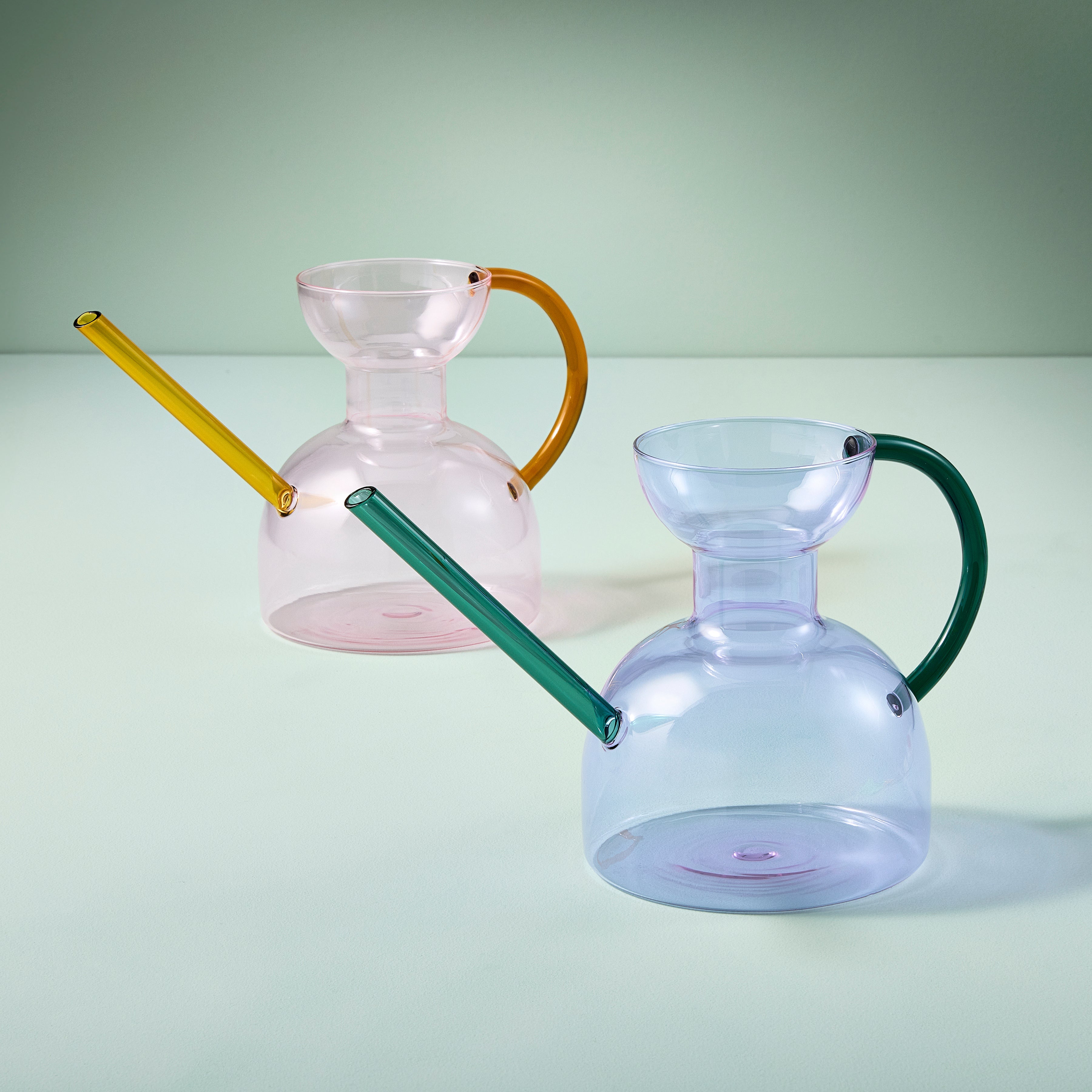 Two glass pitchers with colorful handles on a light green background