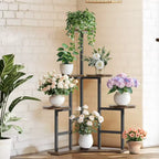 A multi-tiered black metal plant stand with wooden shelves, styled with various potted green plants and bouquets of white, pink, and purple flowers against a white brick wall.