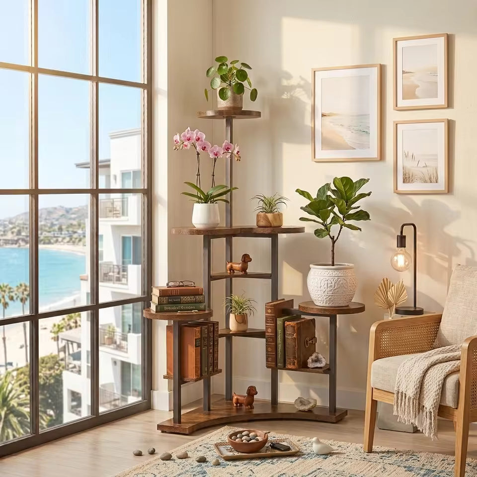 A multi-tier wooden plant and bookshelf stand styled in a bright, modern coastal living room corner with a large window overlooking the ocean.