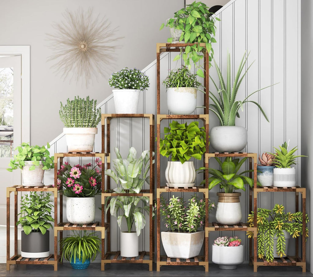 Wooden plant stand with various potted plants against a neutral wall.