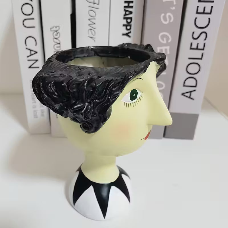 Decorative head with black hair and face on a white surface with books in the background