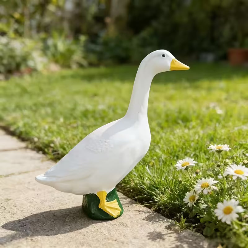 White garden porch goose statue on a stone path with grass and flowers in the background