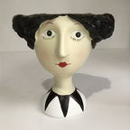 Vase shaped like a woman's head with black hair, white face, and red lips on a plain background
