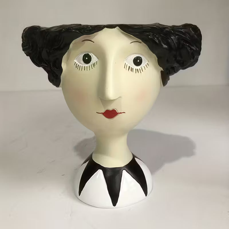 Vase shaped like a woman's head with black hair, white face, and red lips on a plain background
