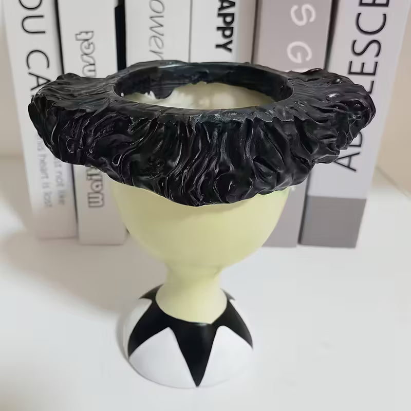 Decorative garden planter with black textured top and white base on a white surface.