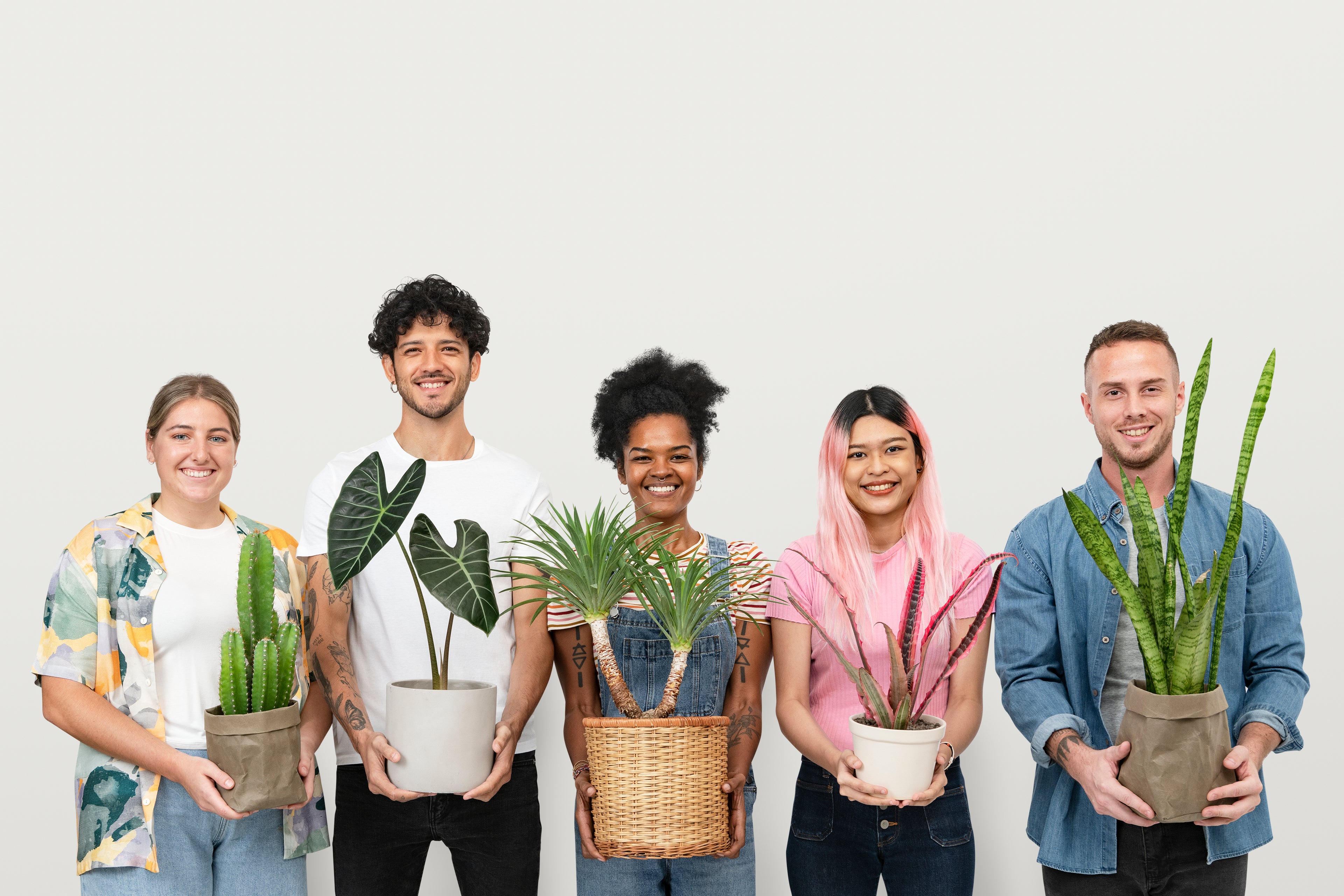 Group of six people holding various potted plants against a white background